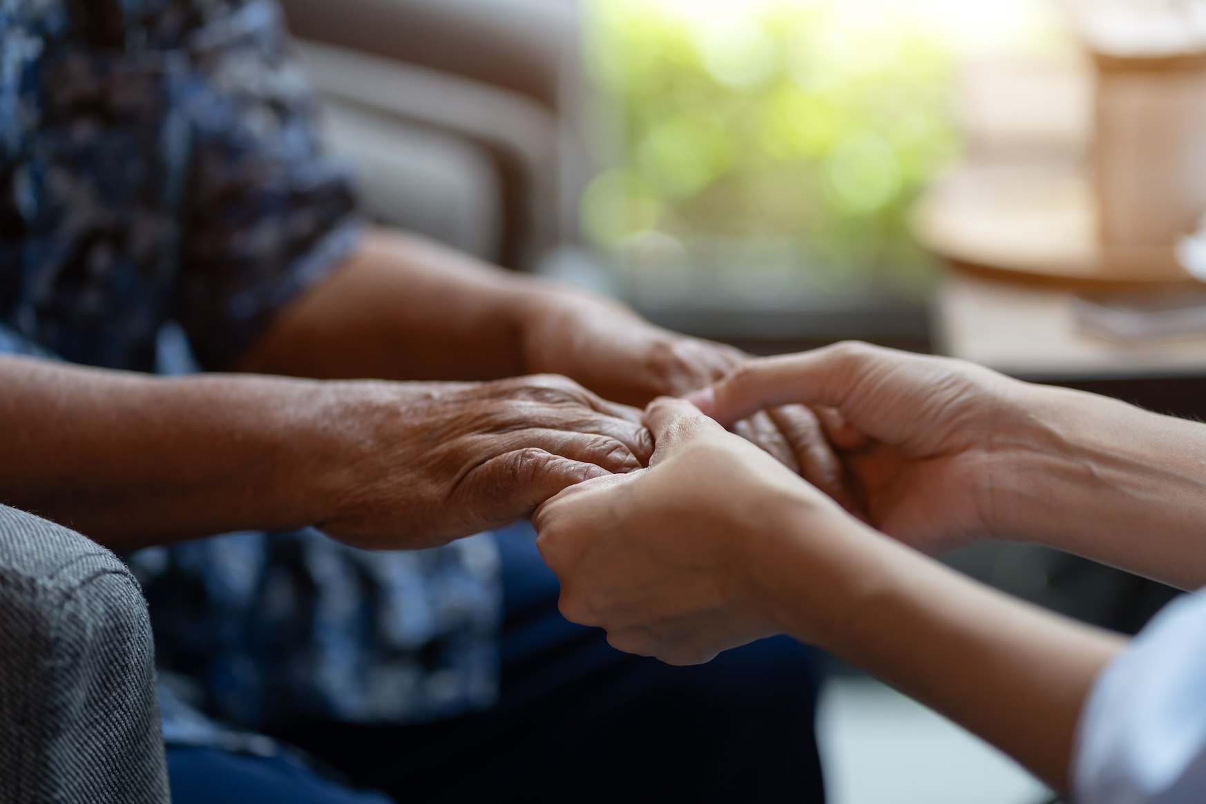 Younger caregiver holds the hands of senior woman in hospice.